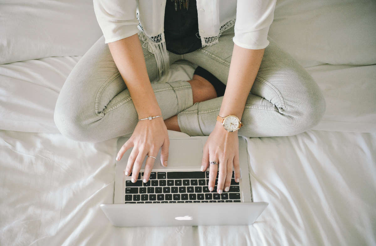 Woman uses macbook sitting cross-legged on her white bed